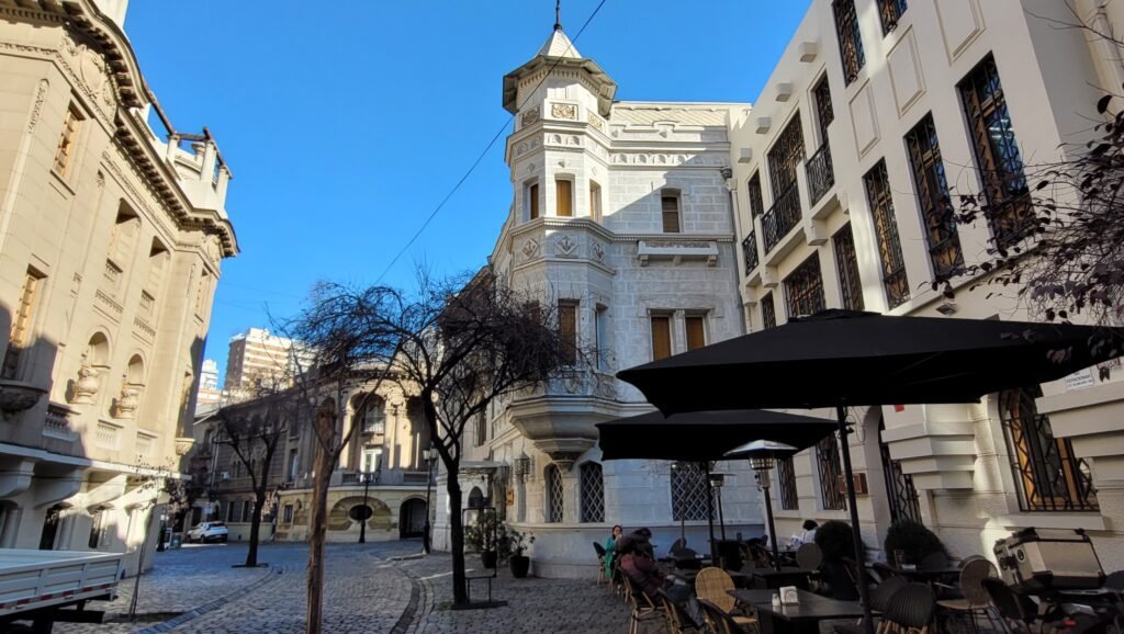 Calle adoquinada en el Barrio Lastarria de Santiago con edificios de arquitectura clásica y mesas de restaurante al aire libre.
