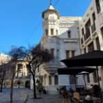 Calle adoquinada en el Barrio Lastarria de Santiago con edificios de arquitectura clásica y mesas de restaurante al aire libre.